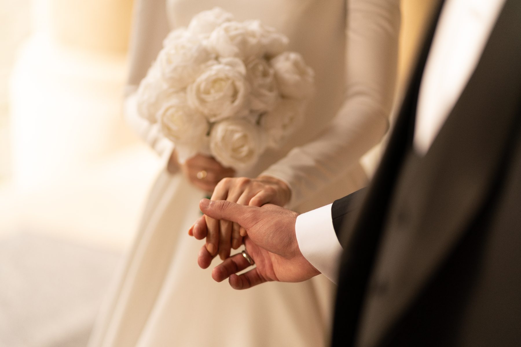Elegant couple holding hands at the altar, the bride holding a white rose bouquet